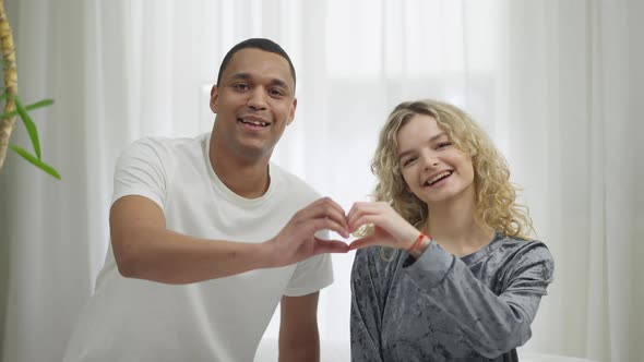 Medium Shot of Happy Smiling Interracial Couple Making Heart Shape with Hands Smiling Looking at