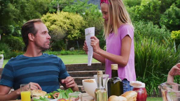 Smiling caucasian girl showing parents her top mark on school work in garden