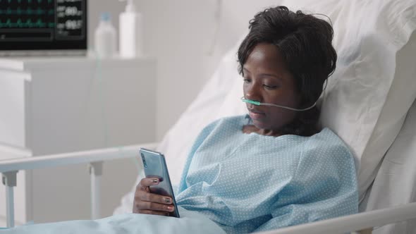 A Young Woman Writes a Message on Her Phone While Lying in a Hospital Ward alt