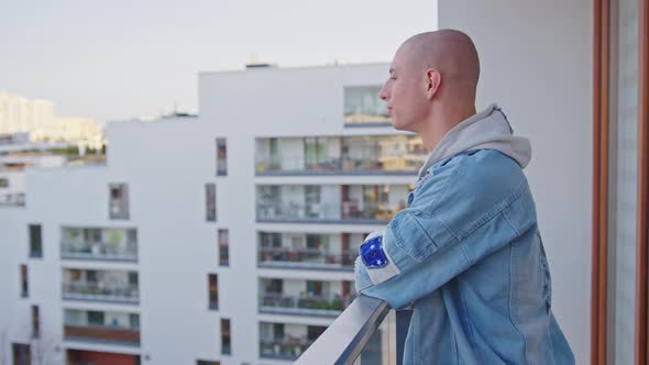 Medium Outdoor Shot of a European Queer Gay Man Standing on His Balcony Looking at the Neighborhood