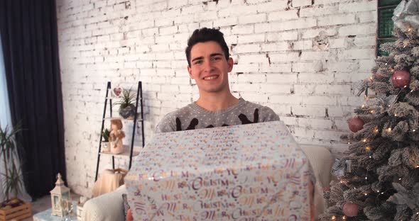 Young Guy Smiling at Christmas Gives a Gift To the Camera