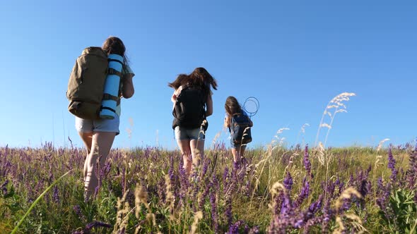 Happy Mom and Daughters, a Little Baby Travel Across the Field with Backpacks in Colors in the