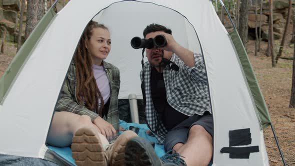 Young Happy Man and Woman Talking and Looking at Forest Through Binoculars Inside Tent on Autumn Day