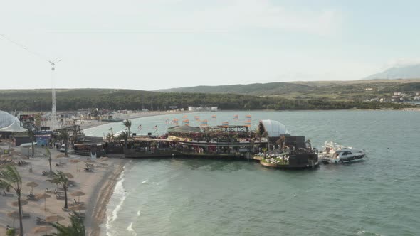 AERIAL: Beautiful Beachclub in Novalja, Croatia at the Ocean with Waves in Sunny Weather and Flags