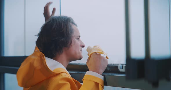Young man looking out of foggy window while smiling and eating a banana