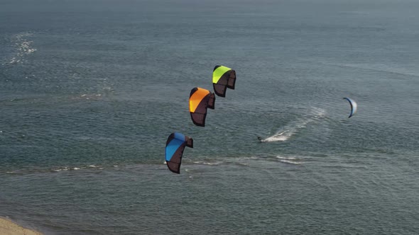 Three multicolored kites hover in front of kitesurfer riding dutch bay; drone
