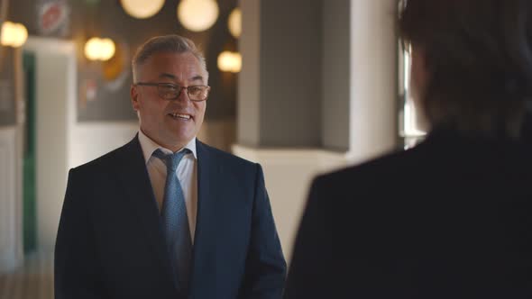 Back View of Successful Senior Businessman Talking To Partner While Waiting in Lobby