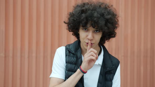 Cheerful Middle Eastern Teenager Touching Lips with Forefinger Asking for Silence and Smiling