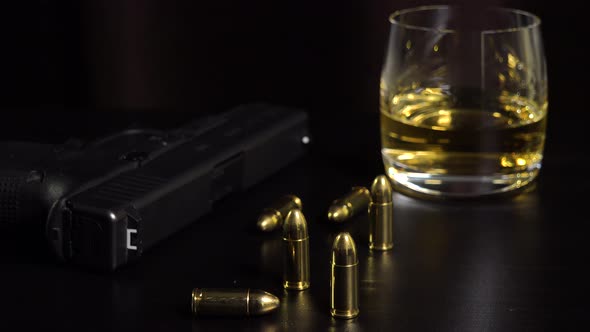 A Glass of Whiskey, a Gun and Bullets on a Black Table - Closeup