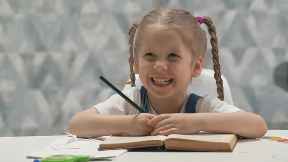 Happy Little Girl Does Homework with Book Sitting at Table