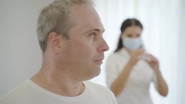 Close-up of Mid-adult Caucasian Man Looking Back at Nurse in Face Mask Preparing Vaccine and Turning
