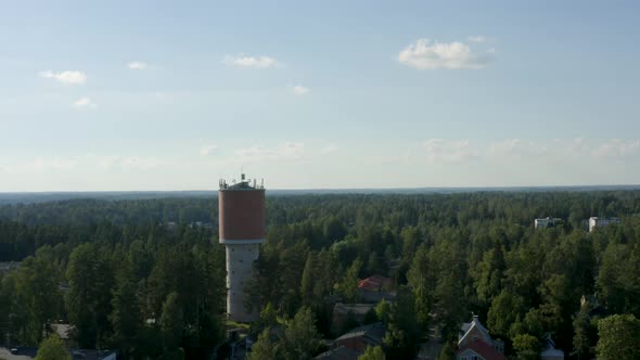 Aerial reversing shot of a large water tower above the trees in Finland.