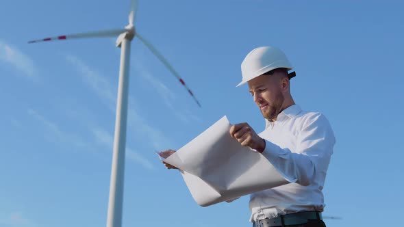 A Male Engineer in a White Helmet and a Classic Shirt Inspects the Power Plant's Capacity and Reads