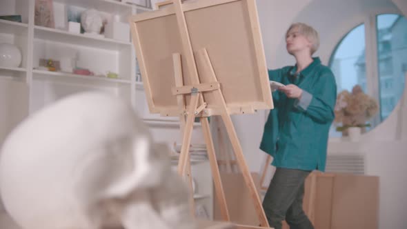 A Young Blonde Woman Artist Drawing a Skull and Other Figures From the Table