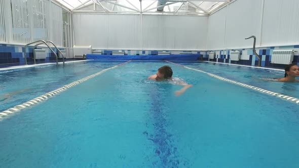 Two Smiling Young Women Swimming in Different Pool Lanes with a Young Man Swimming Crawl