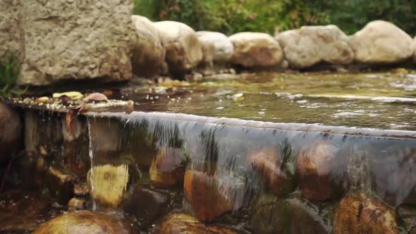 The water of the decorative waterfall flows down the mossy brown stones