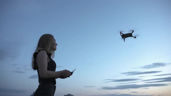 Young girl controlling quadcopter drone flying in the air with remote controller under blue sky in t