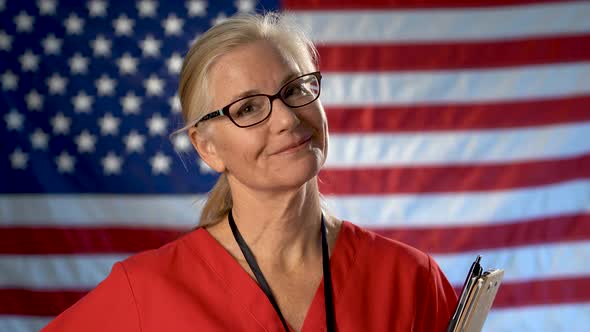 Portrait of a nurse showing a smile and approval set against an out of focus US flag.