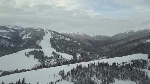 Flight Over a Village in Carpathian Mountains and a Ski Resort Next To It. Bird's Eye View of Snow