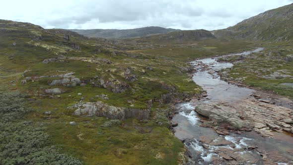 Meltwater river flowing in Norway Hardangervidda valley, aerial side truck view