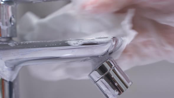 Close-up View of a Woman's Hand Washing the Faucet in the Bathroom Using a Detergent and