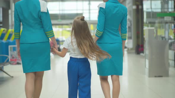 Back View of Happy Caucasian Girl Holding Hands of Professional Stewardesses and Walking To Airport