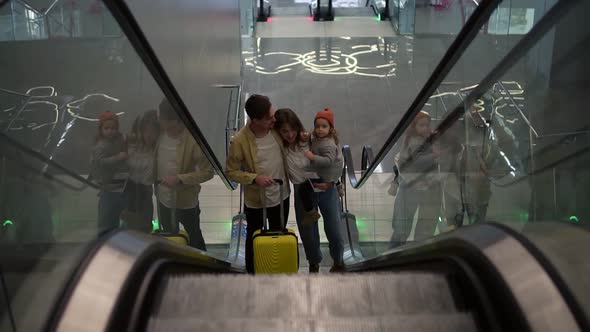 Happy Young Family with Yellow Suitcase Going Up By the Escalator From the Airport Hall