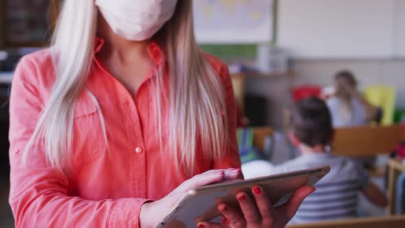 Female teacher wearing face mask using digital tablet at school