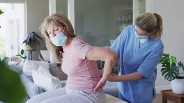 Female health worker stretching back of senior woman at home