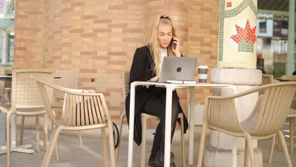 Woman talking on smartphone while working with laptop in cafe