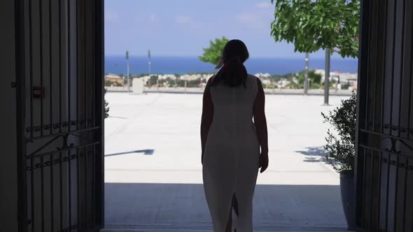 Back View of Happy Caucasian Young Woman in White Dress Walking to Square in Mediterranean Country