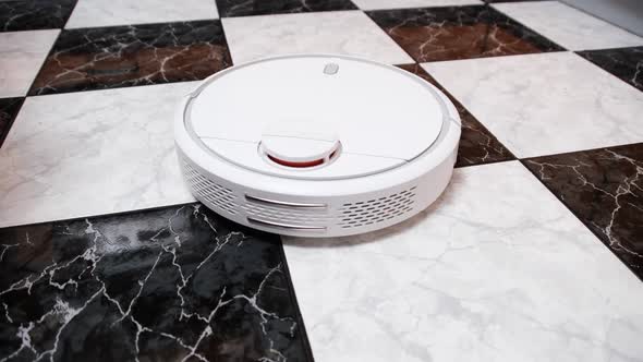 The Robot Vacuum Cleaner Cleans in the Modern House on the Tiles Floor at Kitchen