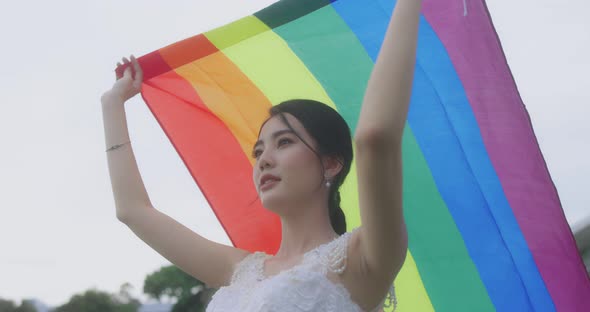 Asian Lesbian Girl Raising LGBT Rainbow Flag In The Park.