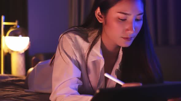 Young Asian beautiful woman enjoy using smartphone- tablet   in bedroom at night time.