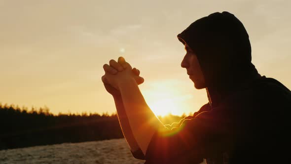 A Young Man in a Hood Prays at Sunset