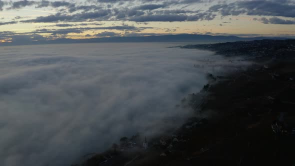 Aerial flying backward revealing sea of fog over Lake Léman at sunset - Switzerland