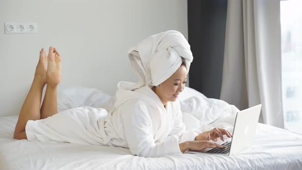 Young Woman Lying in Bed Working Remotely Online on a Laptop Due To the Coronavirus Pandemic Many