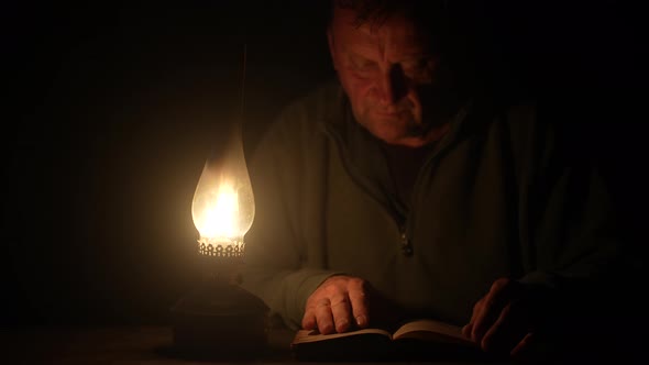 Man reads a book by the light of a kerosene lamp at night time