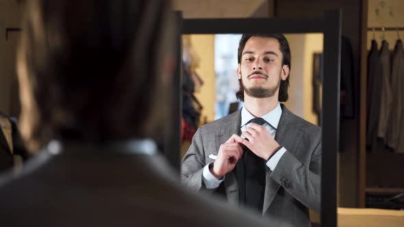 Mirror reflection of young bearded man trying on suit in fashion store.