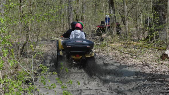 A couple on a yellow ATV riding through mud and puddles in the woods. Back view