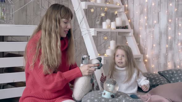 Blond Mother and Daughter Play with Christmas Toys on Bed