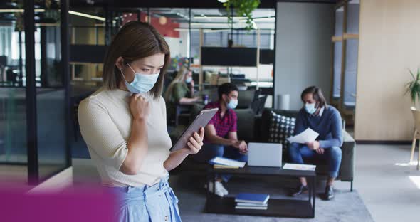 Asian businesswoman wearing face mask using digital tablet modern office