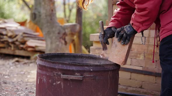 An Artisan Potter carries out maintenance on her brick kiln and cleans the bricks by scraping off ba