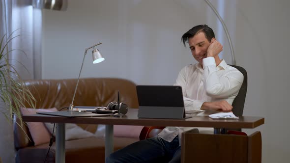 Laughing Handsome Middle Eastern Man Sitting at Table in Home Office Looking at Tablet Screen