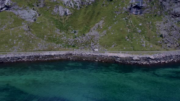 Flying over the ocean looking at a coast road with a campervan driving.