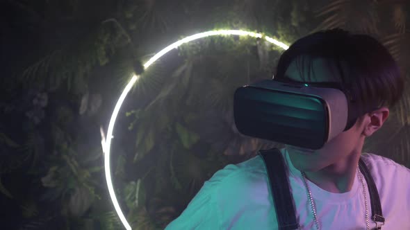 Asian Man Wearing Virtual Reality Glasses Against Neon Light Background