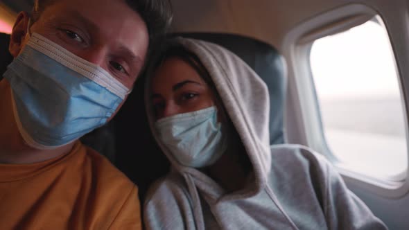 Happy Couple Man and Woman in Medical Safety Mask at Aircraft Cabin Next to Window at Take Off