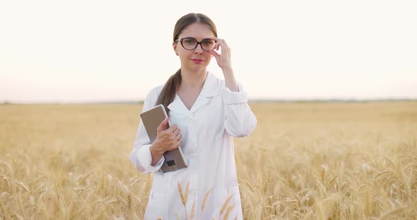 Woman Agronomist Posing at Camera in Wheat Field Holding Grey Tablet and Taking Off Glasses