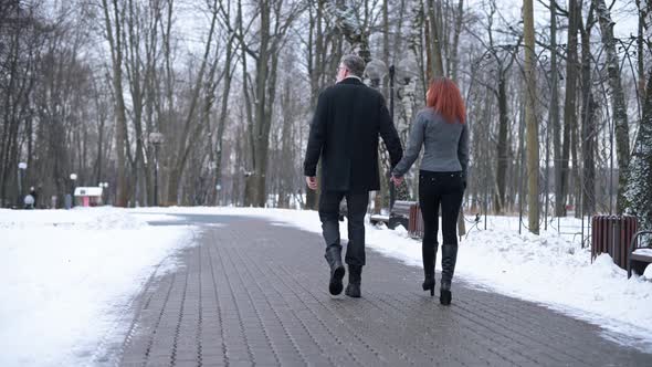 Man and a woman walking in the park. A tall gray-haired man with his girlfriend