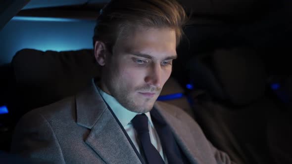 Portrait of a Young Businessman Sitting in a Moving Car and Using Laptop Man Top Manager in a Suit